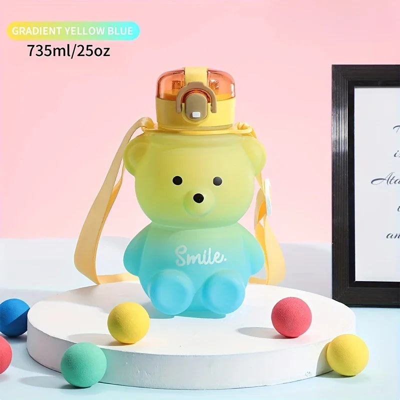 A yellow bear-shaped water bottle with a straw and strap is displayed on a white stand against a pink background.