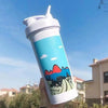 يد تمسك بزجاجة خلط بروتين بيضاء فيروزي أمام سماء زرقاء صافية ومبانٍ بعيدة.