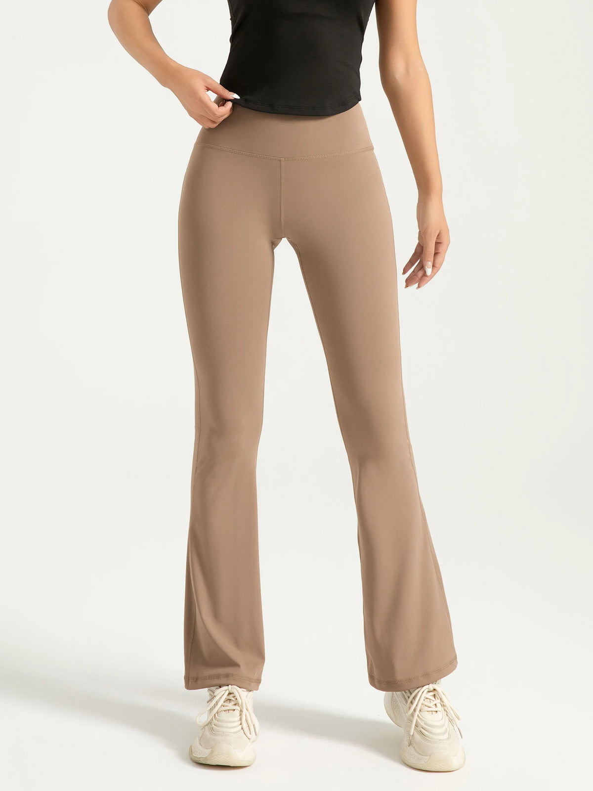 A model wearing high-waisted bootcut yoga pants in a beige color.