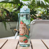 A clear plastic drinking water bottle with a light blue cap and a straw, featuring a cartoon bear and strawberry design.