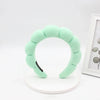 A light green sponge terry cloth headband for hair styling displayed on a white circular stand.