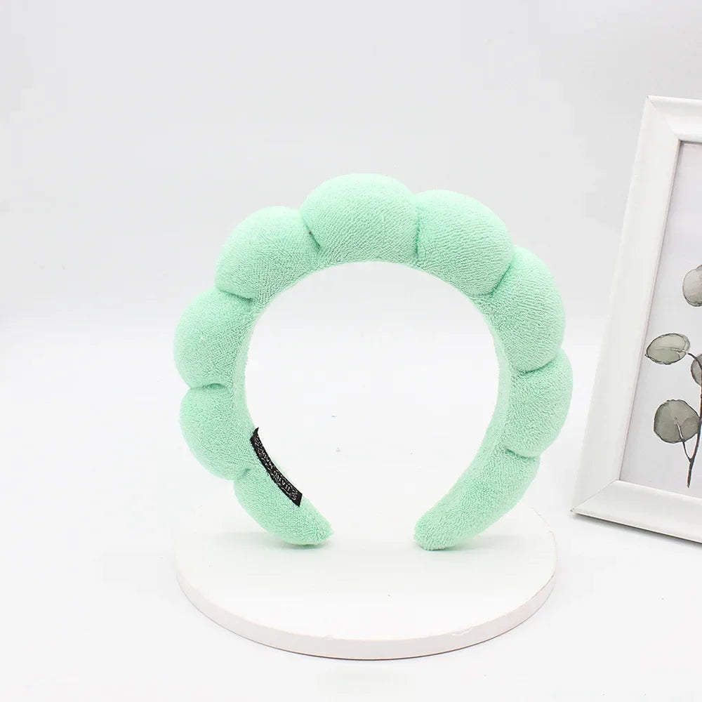 A light green sponge terry cloth headband for hair styling displayed on a white circular stand.