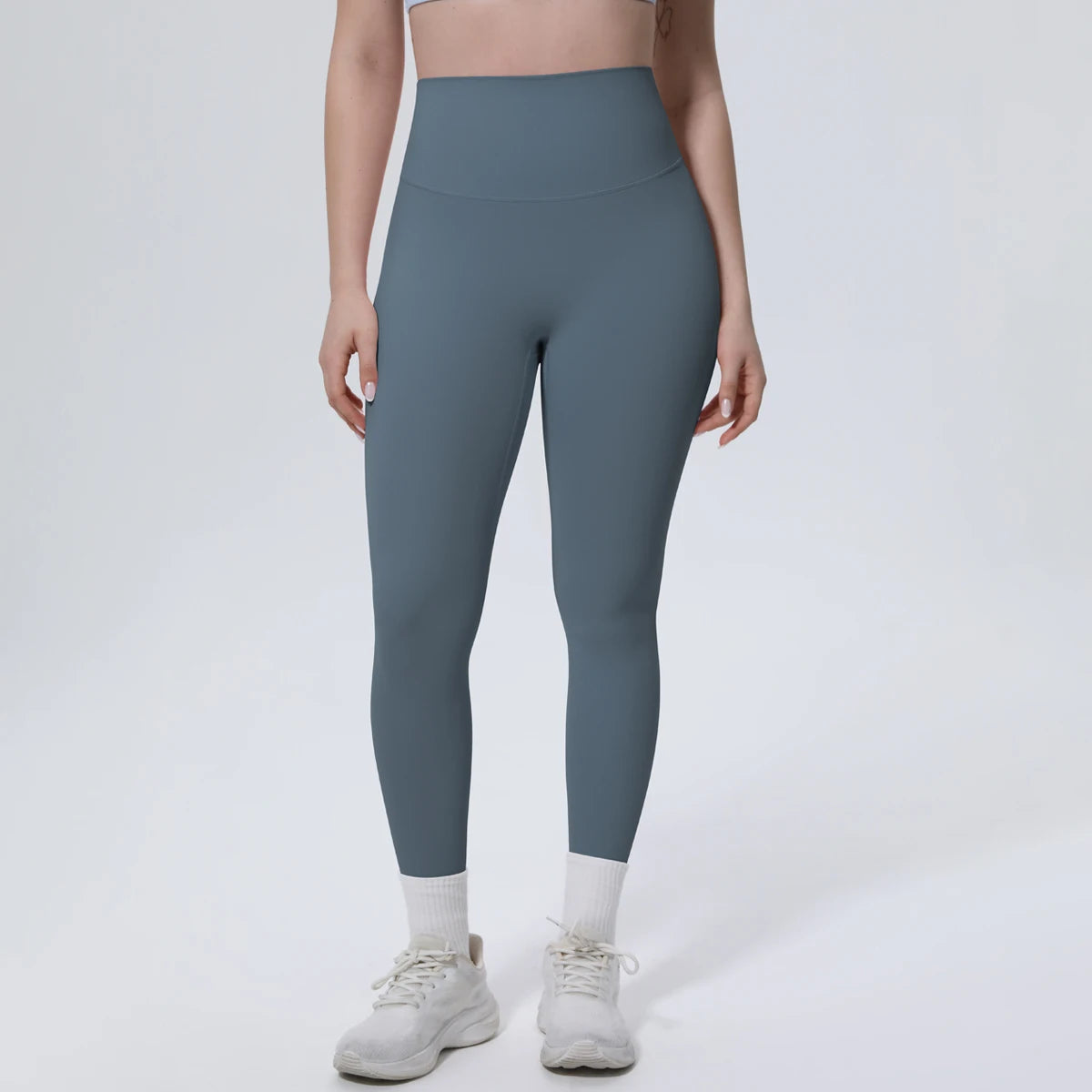 A model wearing high-waisted, full-length, dark blue quick-drying yoga leggings and white athletic shoes.