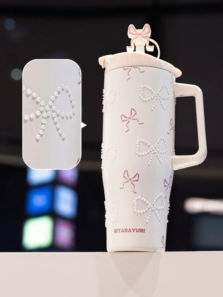A white insulated thermos mug decorated with pink ribbon motifs and pearl inlay, shown next to a matching lid.