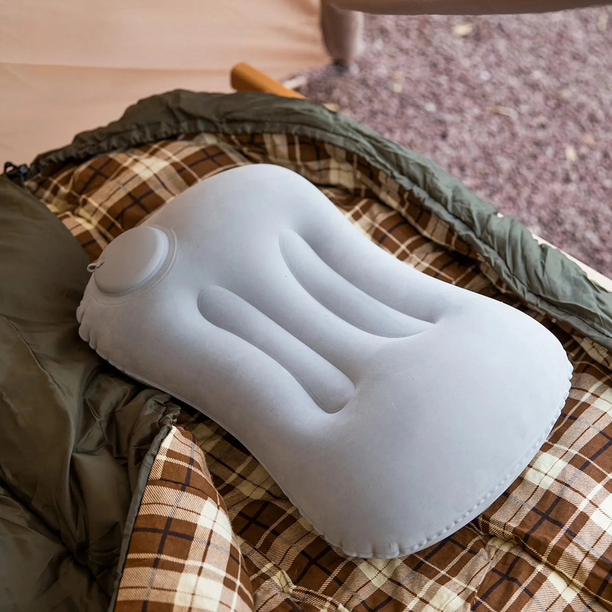 A white inflatable camping pillow is resting on a plaid fabric surface.