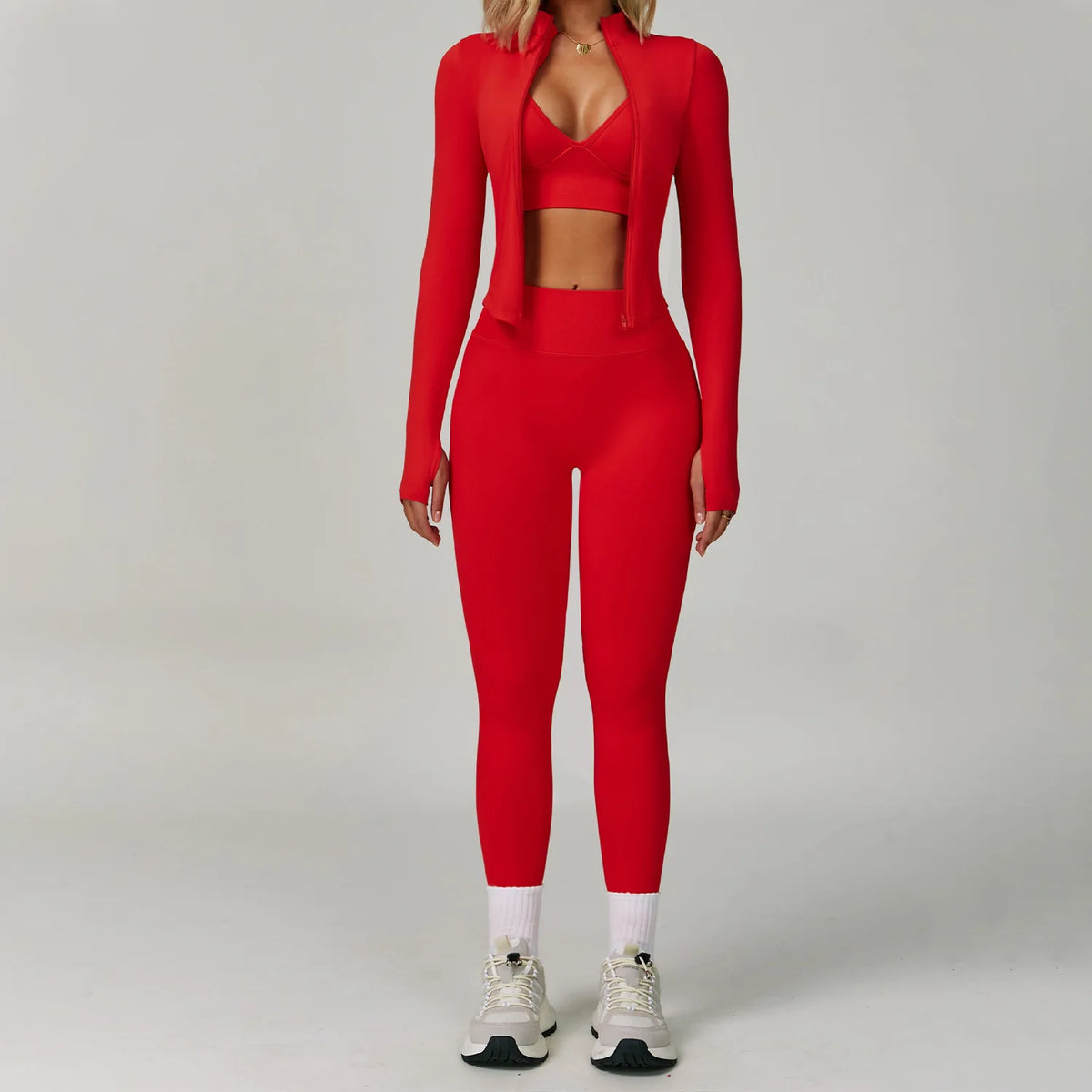Eine Frau in einem roten, nahtlosen Sport-Yoga-Set mit Crop-Top und Leggings vor einem hellgrauen Hintergrund