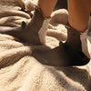 A pair of gray and white knit socks with crocodile detailing resting on a fluffy beige blanket.