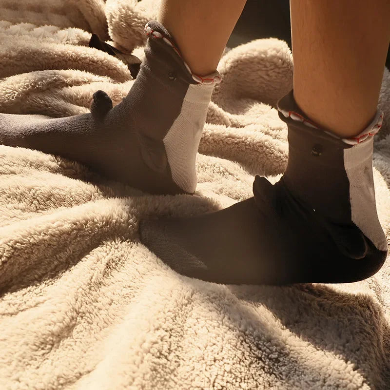 A pair of gray and white knit socks with crocodile detailing resting on a fluffy beige blanket.