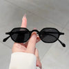 A hand holds a pair of black vintage oval sunglasses with UV400 protection against a light gray background.