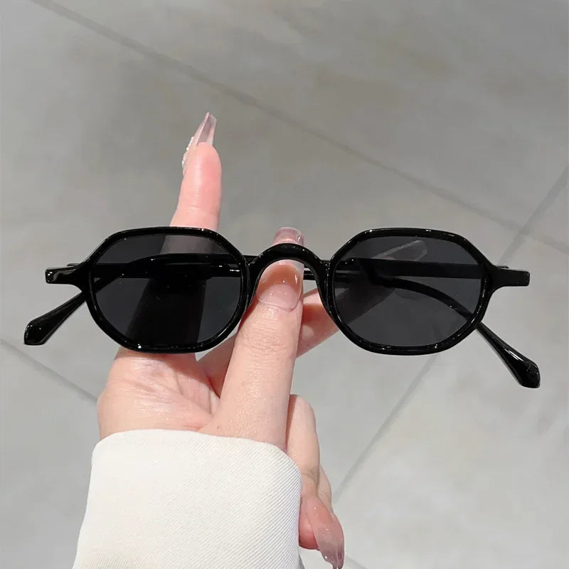 A hand holds a pair of black vintage oval sunglasses with UV400 protection against a light gray background.