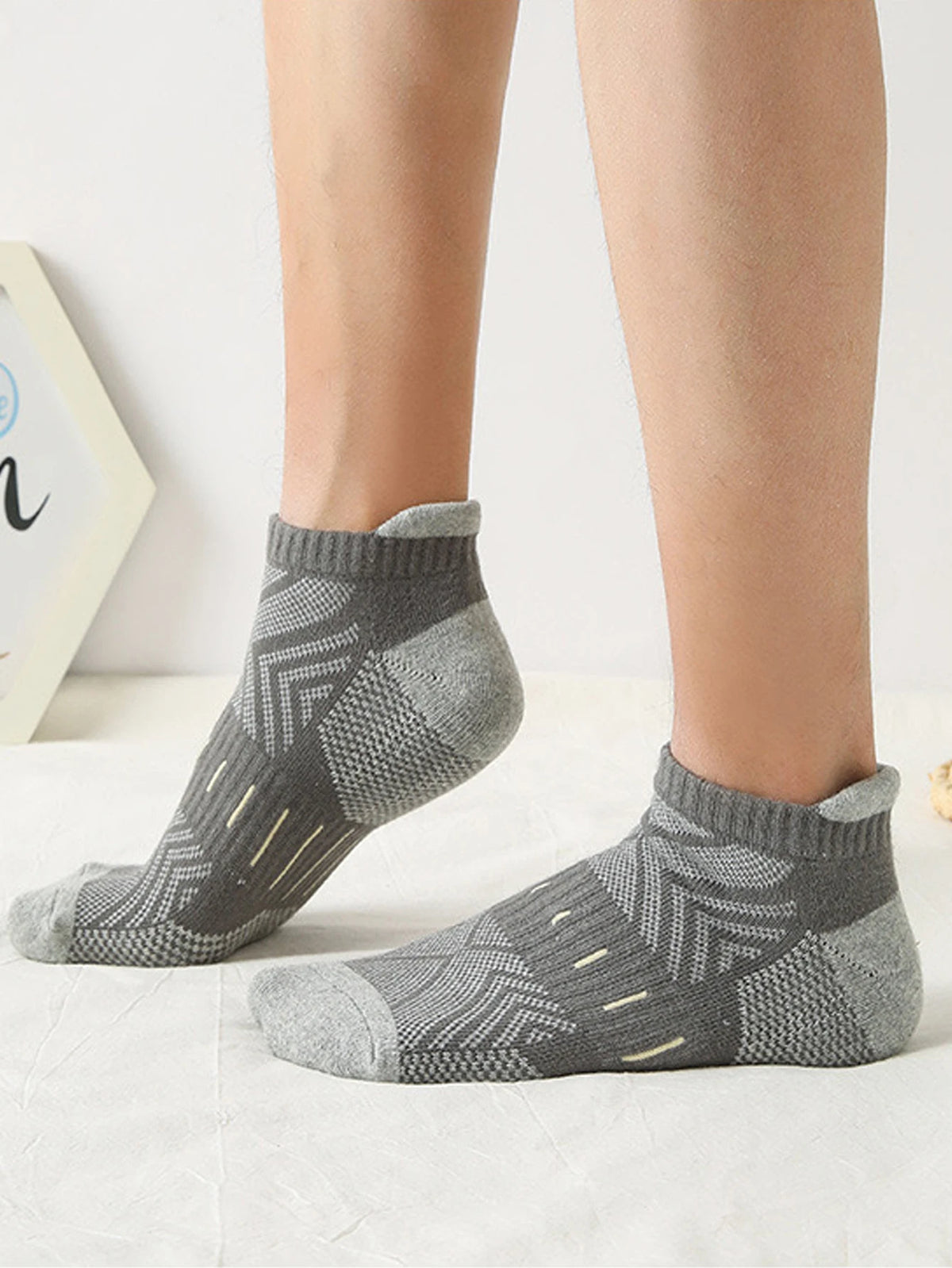 A pair of gray athletic mesh ankle socks with a geometric pattern shown on a person's foot.
