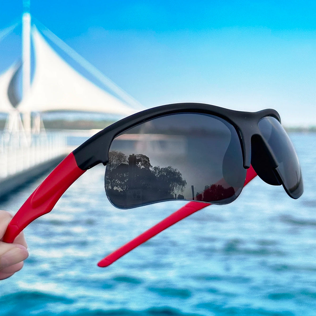 A person holds a black and red sports sunglass with a flexible arm against a bright blue water background.