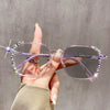 A hand holds a pair of pink photochromic diamond style eyeglasses with purple accents against a gray background.