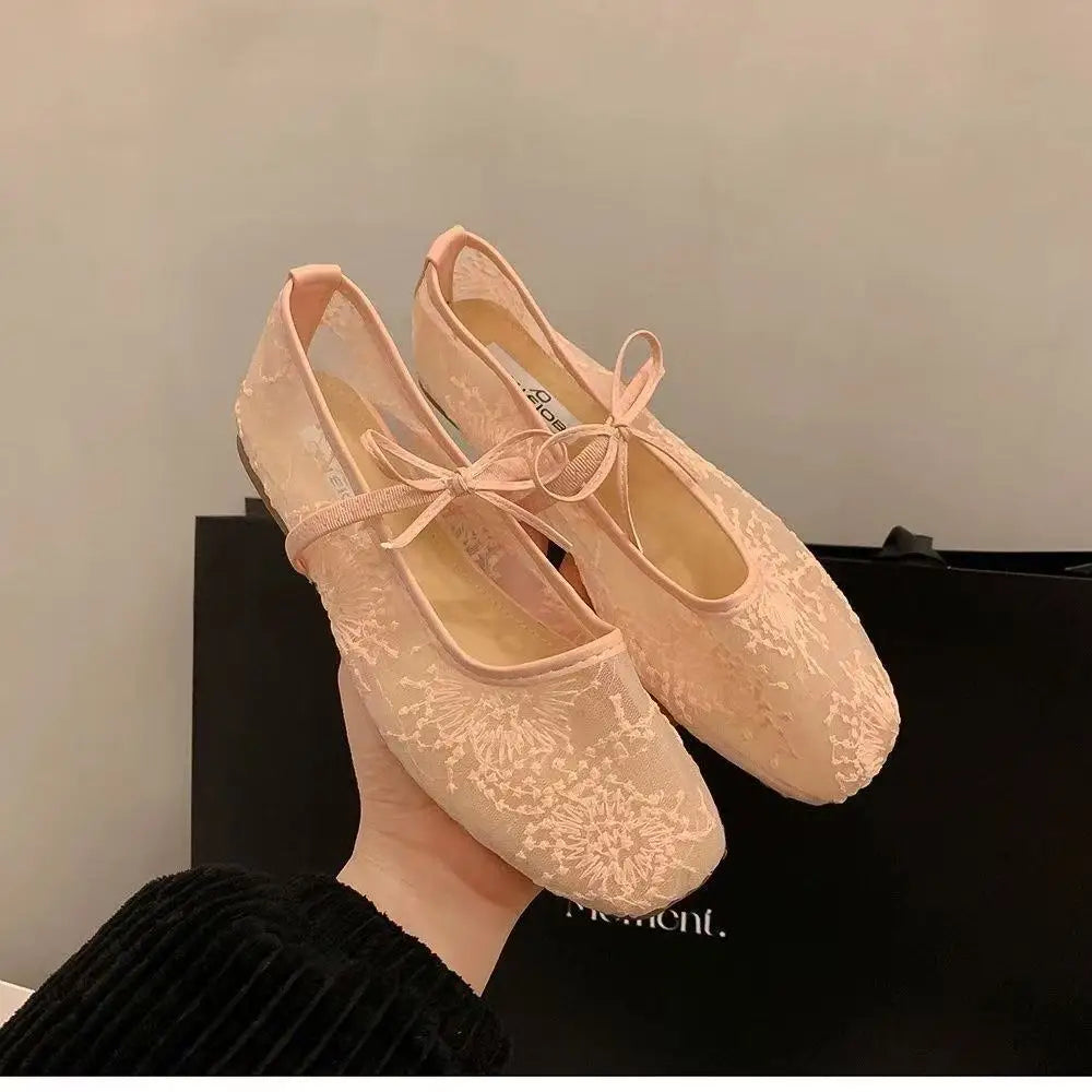 Un par de elegantes bailarinas de encaje en color melocotón pálido contra un fondo negro.