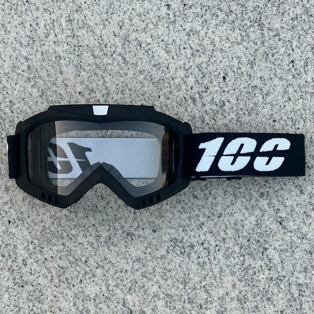 Black heavy-duty motorcycle and ATV goggles with a white strap resting on a gray surface.