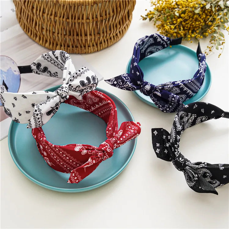 A collection of paisley bandana fabric headbands in white, red, and navy blue laid out on a light surface.
