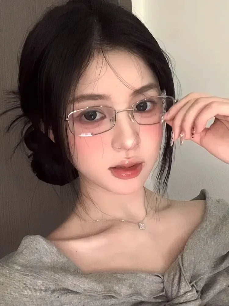 A close-up portrait of a woman wearing retro square frame eyeglasses against a light background.