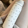 A white insulated stainless steel sports water bottle is held in a hand against a light background.