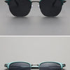 A pair of dark green metal frame sunglasses with black lenses shown against a light gray background.