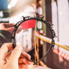 Una mano sostiene un set de clips y diadema para flequillo doble color negro contra un fondo desenfocado.