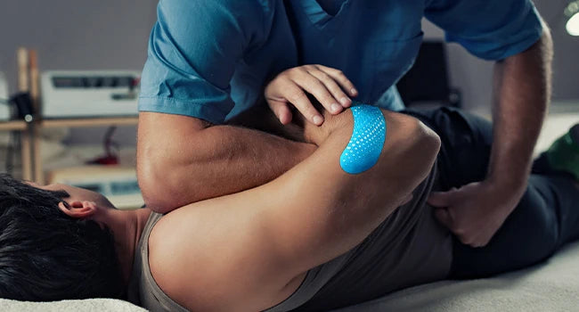 A person applies a blue kinesiology tape to their elbow or knee during a physical therapy or exercise session.