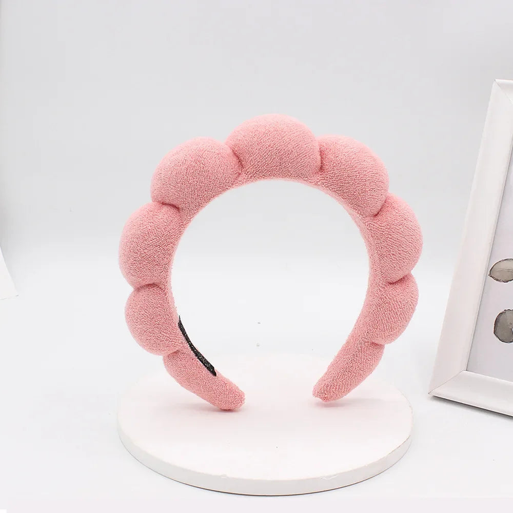 A pink sponge terry cloth headband for hair styling displayed on a white circular stand.