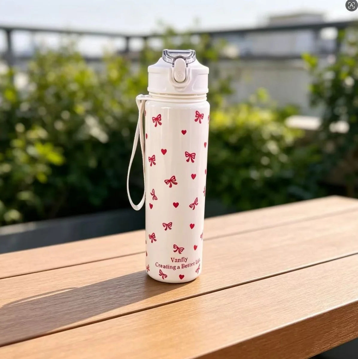 A white reusable water bottle with a strawberry bow pattern sits on a wooden table outdoors.