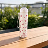 A white reusable water bottle with a strawberry bow pattern sits on a wooden table outdoors.