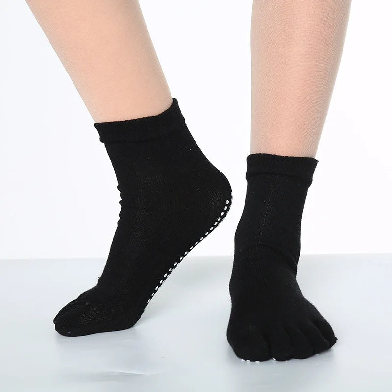 A pair of black rainbow yoga socks worn on a person's feet.