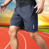 A man wearing dark blue quick dry jogging shorts is running on a red track at sunset.