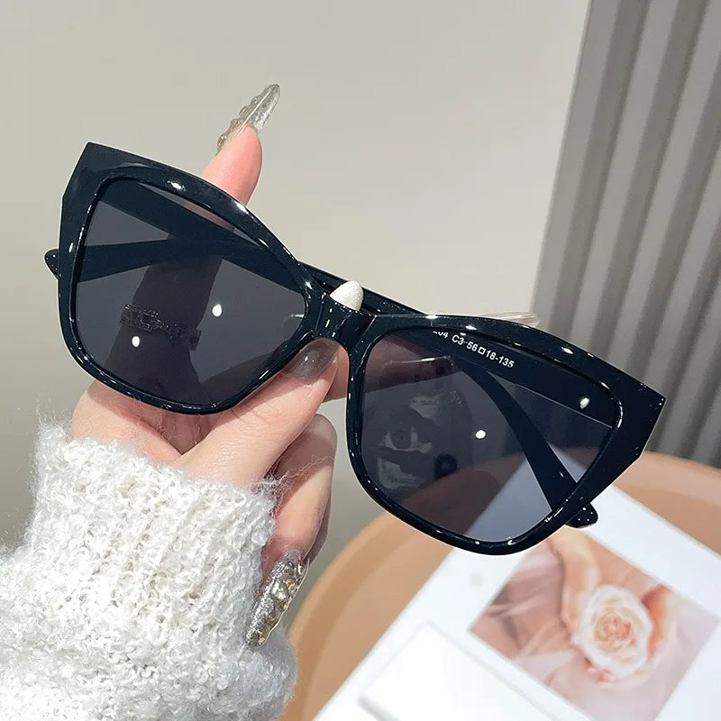 A hand holds a pair of black vintage square cat eye sunglasses with UV400 protection.