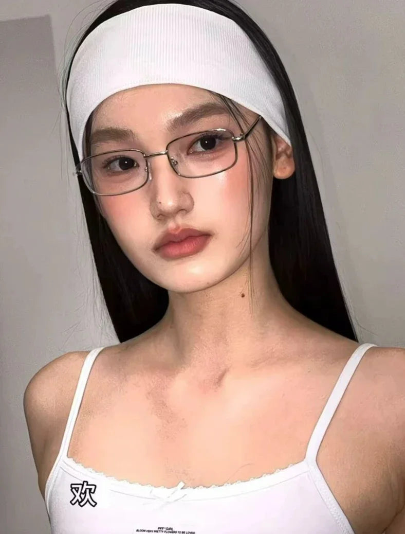 A close-up of a woman wearing white retro square frame eyeglasses and a white headband.