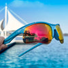 A close-up of blue sports sunglasses with polarized lenses reflecting a sunset over water and sailboats.