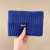 A hand is holding a dark blue knitted headband with the brand name GRANK visible on the inside.
