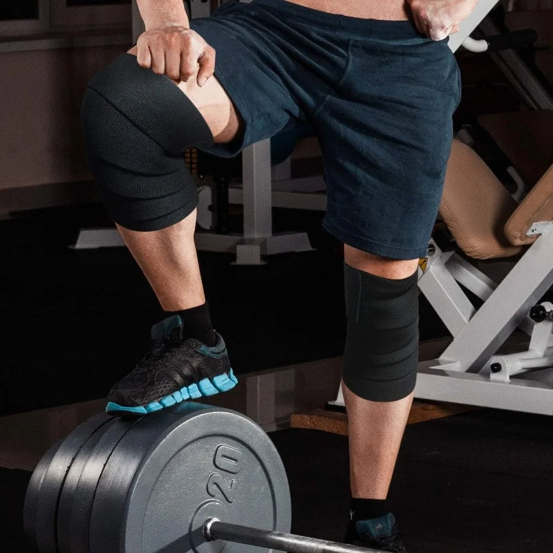 A person wearing dark athletic shorts and knee wraps is performing a strength training exercise with a weight plate.