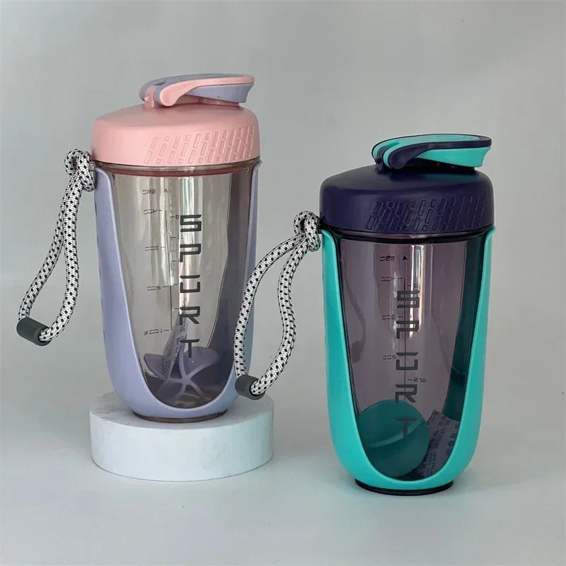A purple blender shaker bottle with a pink lid and a teal colored bottle is shown on a white stand.