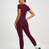 Eine Frau modelliert ein sportliches Yoga-Set in tiefem Bordeauxrot mit kurzem Oberteil und Leggings.