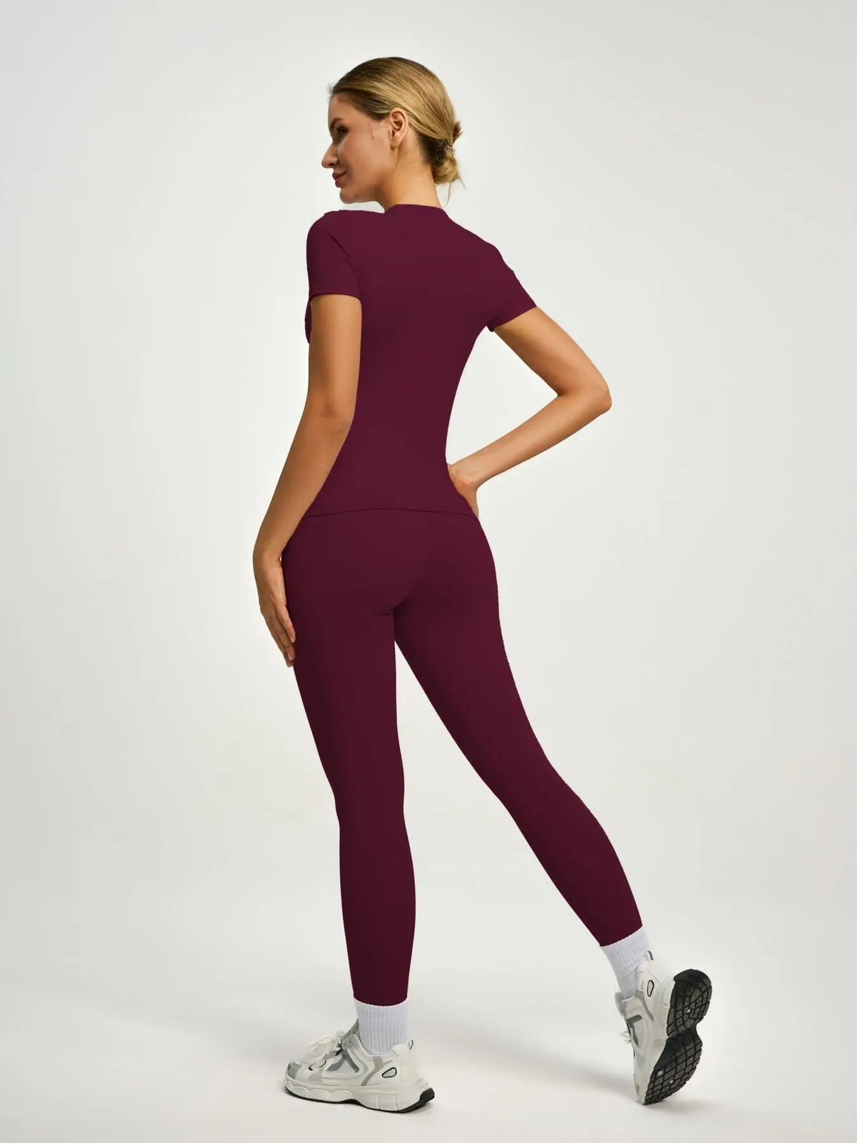 Eine Frau modelliert ein sportliches Yoga-Set in tiefem Bordeauxrot mit kurzem Oberteil und Leggings.