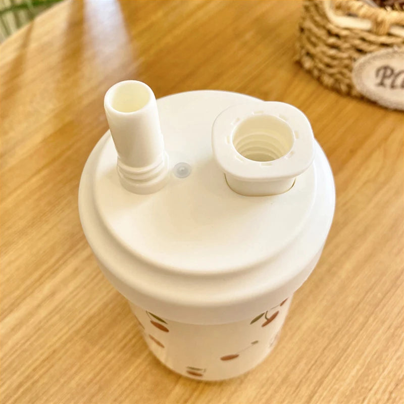 Un tumbler isotherme blanc avec un couvercle à paille est montré sur une surface en bois.