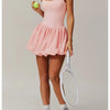 Eine Frau in einem pinken Turnkleid und grauen Sportschuhen, die einen Tennisschläger hält.