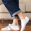 A close-up of a person wearing light gray and white breathable ankle socks with beige canvas sneakers.