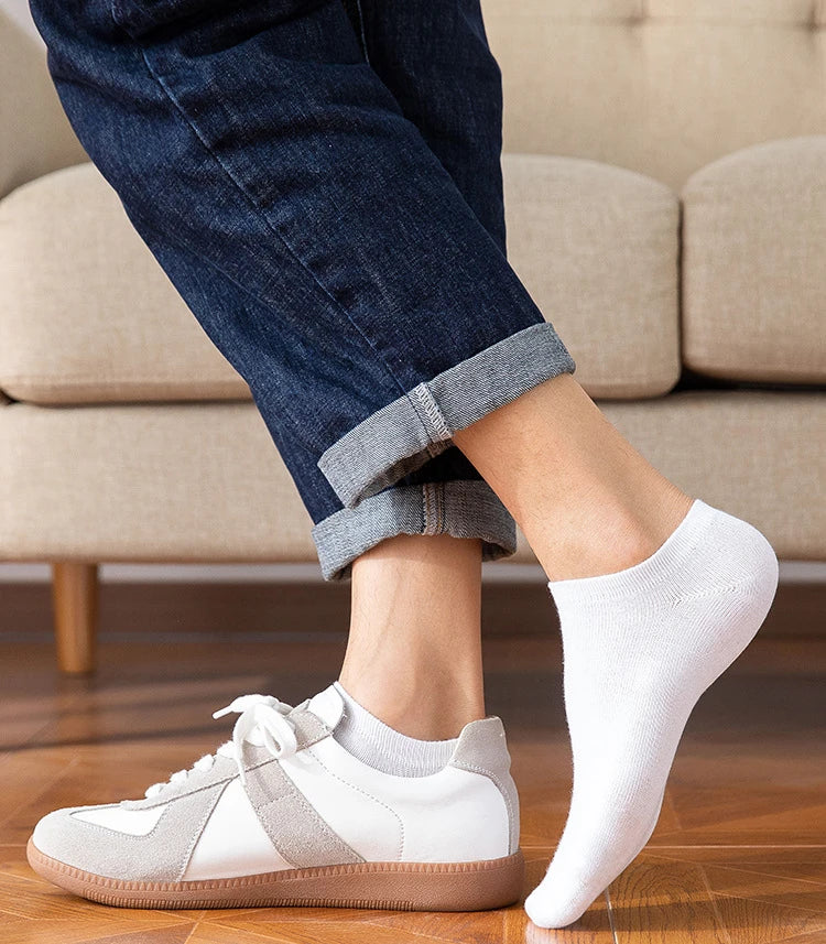 A close-up of a person wearing light gray and white breathable ankle socks with beige canvas sneakers.