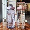 Una botella de agua de vidrio transparente con tapa y pajita rosa sobre una mesa de madera.