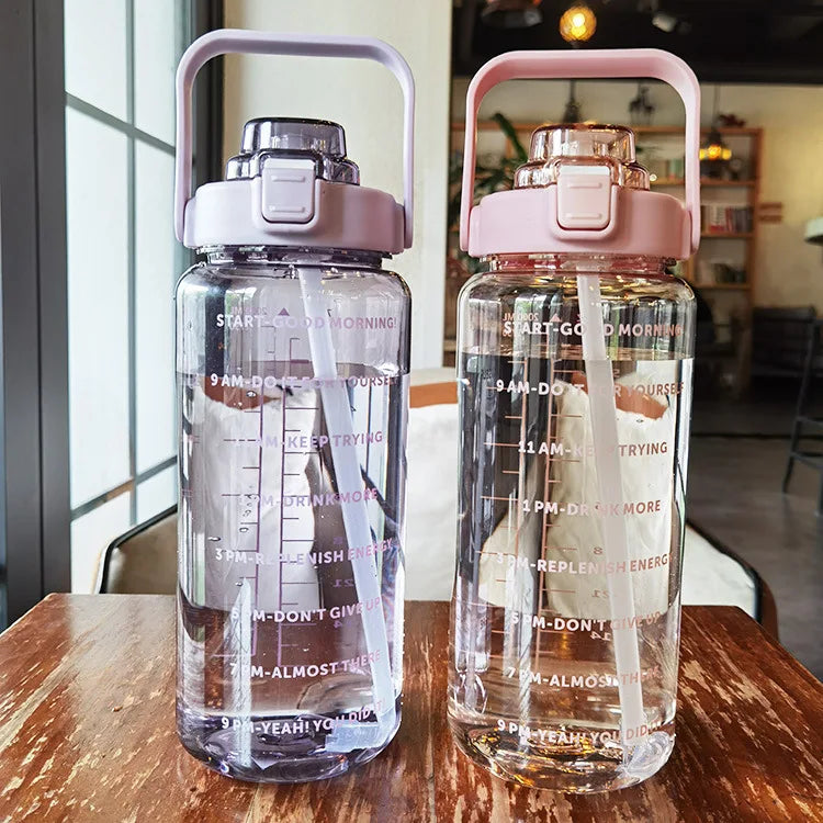 Una botella de agua de vidrio transparente con tapa y pajita rosa sobre una mesa de madera.