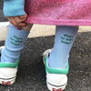 A person wearing light blue knitted socks with embroidered text on their legs and pink fabric.