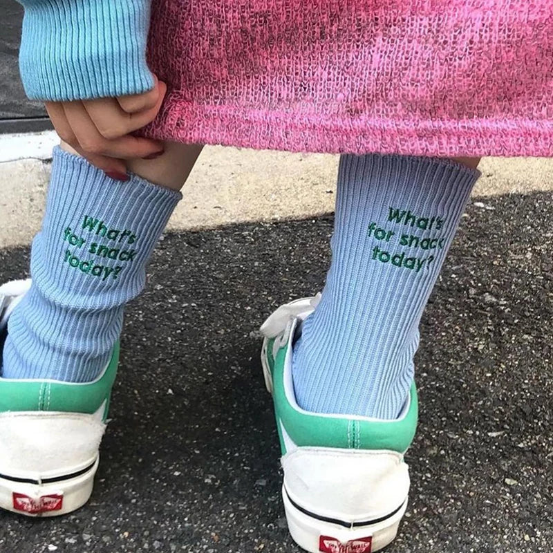 A person wearing light blue knitted socks with embroidered text on their legs and pink fabric.