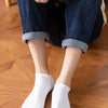 A pair of white breathable men's sports ankle socks worn by a person, paired with dark blue jeans and a beige top.