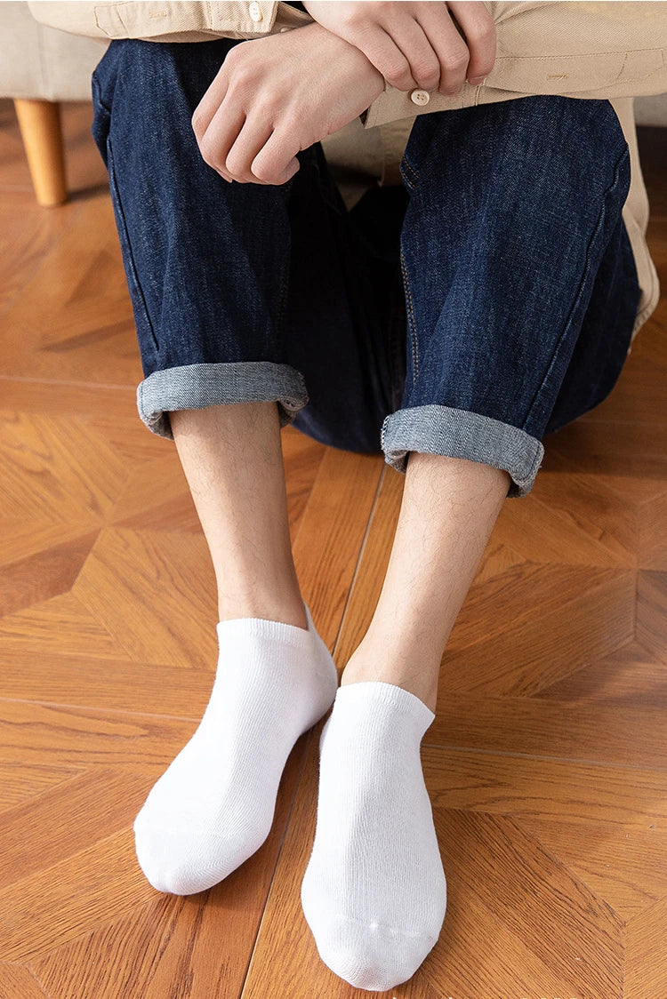A pair of white breathable men's sports ankle socks worn by a person, paired with dark blue jeans and a beige top.