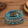 Une pile de cinq bracelets de perles turquoise bohèmes sur une surface en bois.