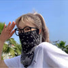 Una mujer vistiendo una bufanda protectora con estampado paisley negro y máscara UV contra un cielo azul brillante.